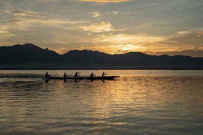 Silhouette people rowing in lake against sky during sunset