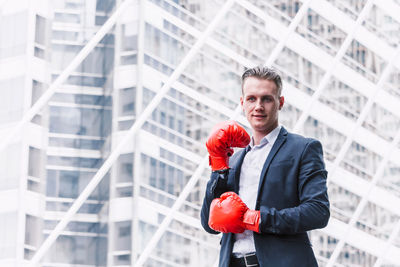 Young businessman wearing boxing gloves while standing against building in city
