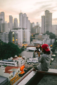 Woman photographing city buildings against sky