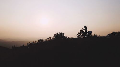 Silhouette person riding bicycle against sky during sunset