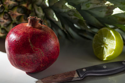 Close up shot of a pomegranate, sliced lime, pineapple and knife