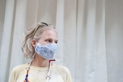 Calm middle aged female wearing protective mask standing on street and looking away during coronavirus epidemic