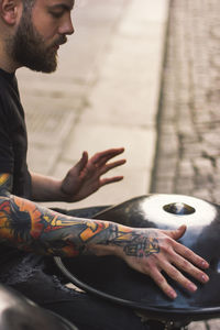 Man playing hang while sitting on city street