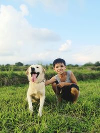 Portrait of boy with dog on grassy land against sky