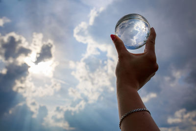 Cropped hand of woman holding crystal ball against sky