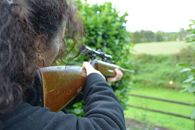 Cropped image of woman holding rifle aiming against trees at park