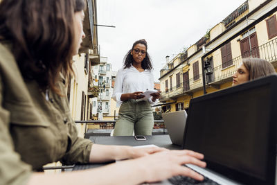 Colleagues listening to businesswoman standing while working on terrace