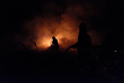 Silhouette firefighters against sky at night