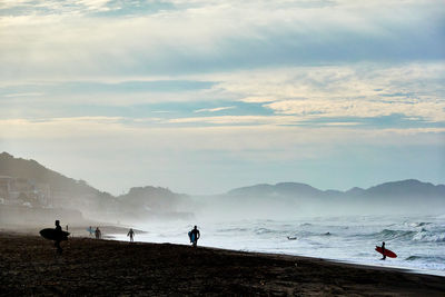 People on beach against sky during foggy morning