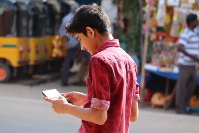 Young boy or man holding mobile phone while standing on street,travel and adventure concept
