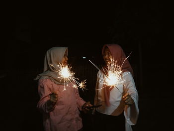 Young woman with friend holding illuminated sparklers at night