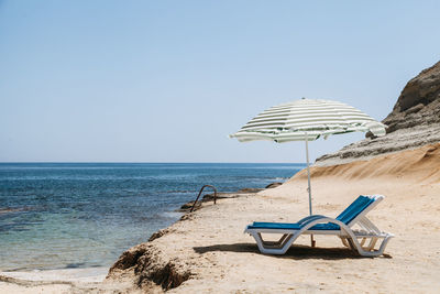 Deck chairs under parasol at beach against clear sky