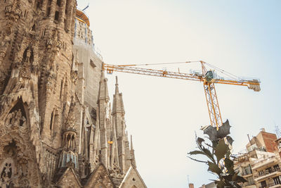 Low angle view of crane by building against sky