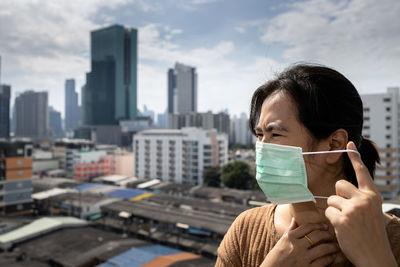 Woman wearing mask looking away against buildings