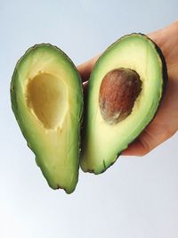 Cropped image of hand holding avocado against white background