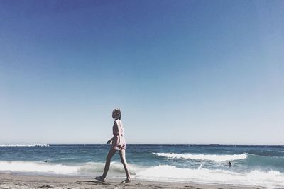 Side view of mid adult woman walking at beach against clear sky during sunny day