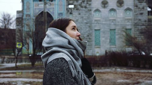 Side view of young woman in warm clothing looking up while walking on street