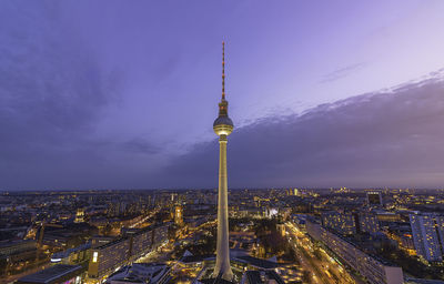Illuminated television tower - berlin amidst buildings against sky during sunset