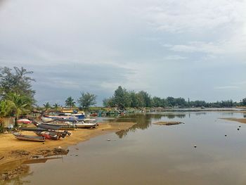 Boats on river by trees against sky