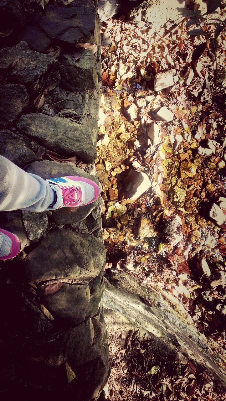 low section, shoe, person, high angle view, standing, lifestyles, footwear, men, leisure activity, rock - object, outdoors, human foot, jeans, day, sunlight, stone - object, dirt, field