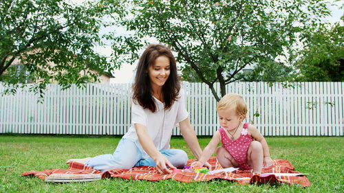 A young beautiful mother playing with a one-year-old daughter, in the garden, sitting on a plaid, a