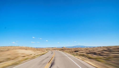 Road passing through desert against clear blue sky