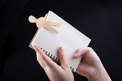 Cropped hand of person holding book against black background