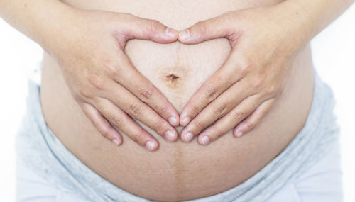 Midsection of pregnant woman making heart shape with hands on abdomen