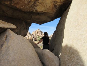 Rear view of woman standing on rock formation against sky