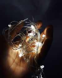 Close-up of hand holding illuminated string lights against black background