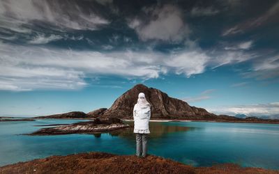 Rear view of woman standing by lake against sky