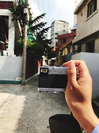 Midsection of man photographing in city against sky