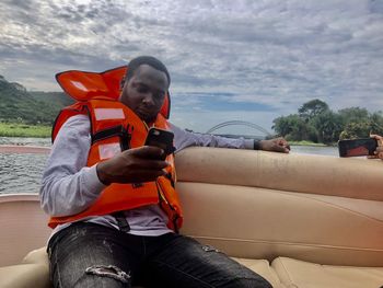 Man using mobile phone while sitting against sky