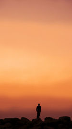 Silhouette man standing on rock against orange sky