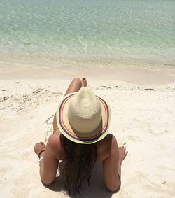 Rear view of sensuous woman wearing hat while sitting on shore at beach