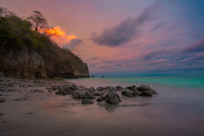 Rocks on beach against sky during sunset