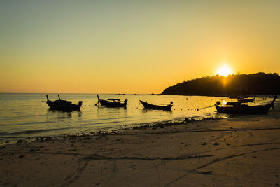 Silhouette boats on beach against sky during sunset
