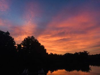 Silhouette trees by lake against romantic sky at sunset