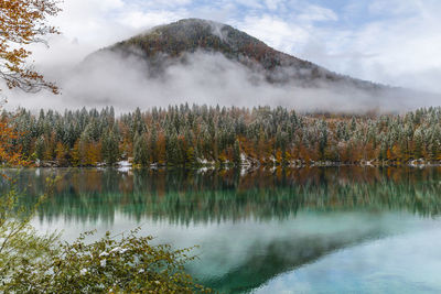 Between autumn and winter. warm and cold reflections of snow on lake fusine.