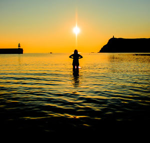 Silhouette man in sea against sky during sunset