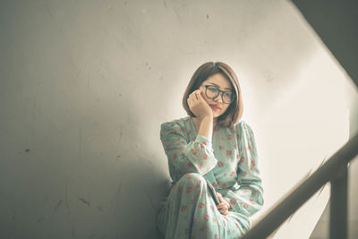 Young woman sitting against wall