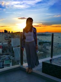 Mid adult woman standing on building terrace against sky during sunset