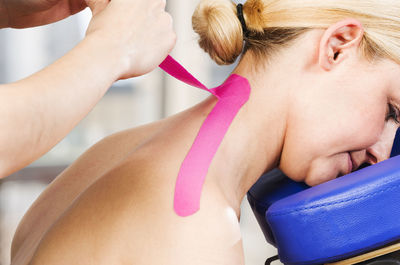 Cropped hands of physiotherapist applying pink kinesio tape on mature woman neck