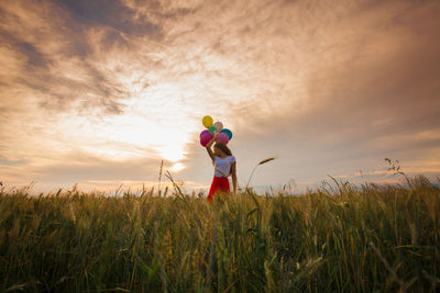 Girl with balloons in grass during sunset