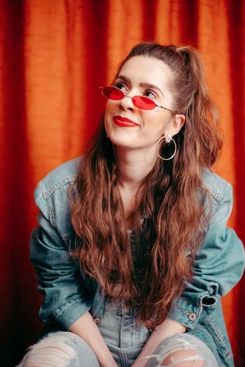 Woman in sunglasses sitting against red curtain