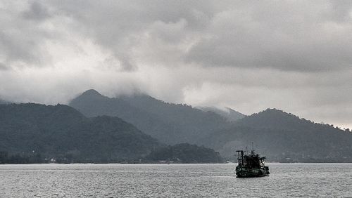 Boat sailing on sea by mountains against sky