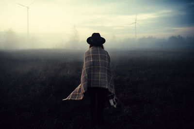 Rear view of woman standing on field in foggy weather