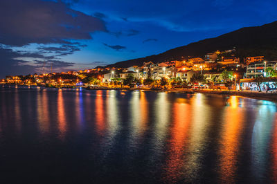 Illuminated buildings by sea against sky at night