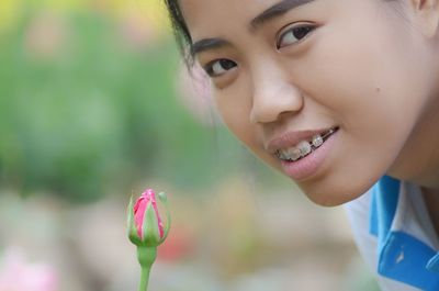 Close-up portrait of young woman with pink flower bud