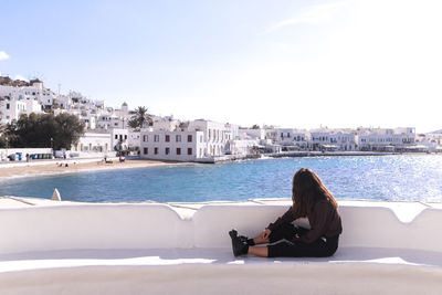 Woman sitting on shore by sea against sky